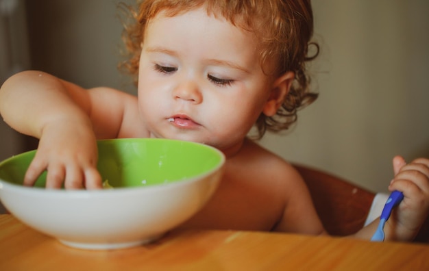 Kid baby come sopa en la cocina con platos y cuchara