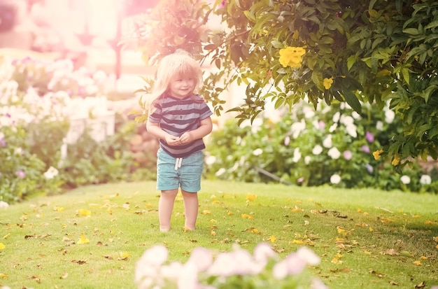 Kid Baby im Freien im Garten mit Blumen und grünem Gras auf natürlichem Hintergrund Sommer Kinder Urlaub Kindheit und Glück