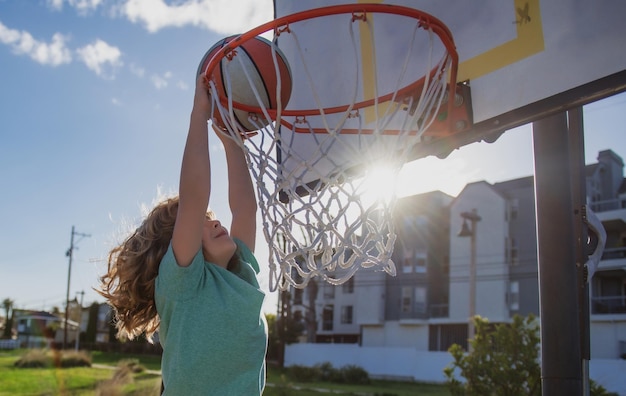 Kid Boy Basketball-Spieler mit einem Ball ein Tor erzielen Child Player Slam Dunk Stock Foto im Freien auf dem Spielplatz