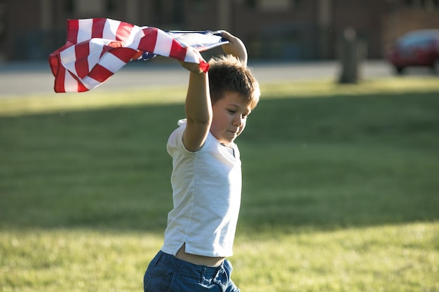 Kid boy celebrando el 4 de julio Día de la Independencia de los EE. UU. Niño corriendo con el símbolo de la bandera americana de los Estados Unidos sobre el campo de trigo