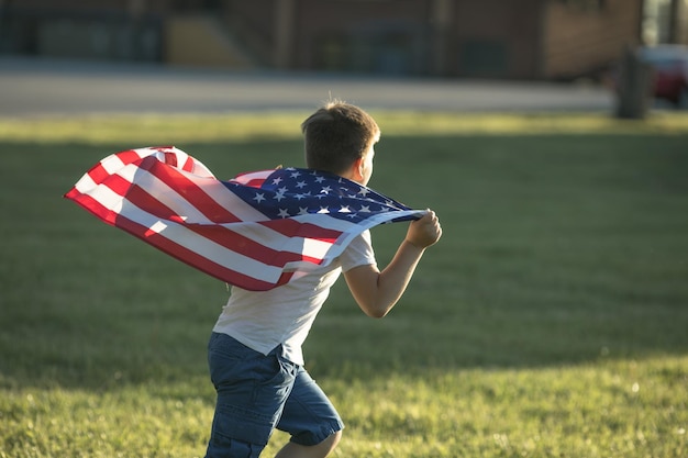 Kid boy celebrando el 4 de julio Día de la Independencia de los EE. UU. Niño corriendo con el símbolo de la bandera americana de los Estados Unidos sobre el campo de trigo