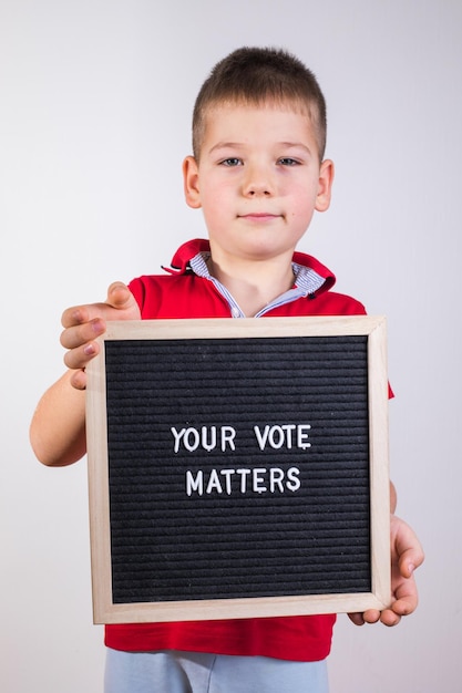 Kid boy holding letter board con texto Your Vote Matters sobre fondo blanco.