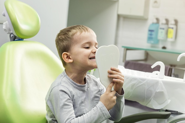 Kid boy en la silla del dentista se mira en el espejo Problema dental