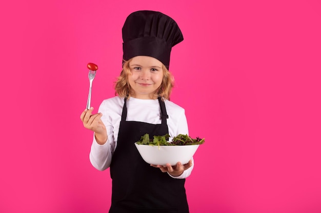 Kid Cook Hold Teller mit Gemüse und Gabel mit Tomate Chef Kind bereitet gesundes Essen zu Studioporträt des Kindes mit Kochmützen