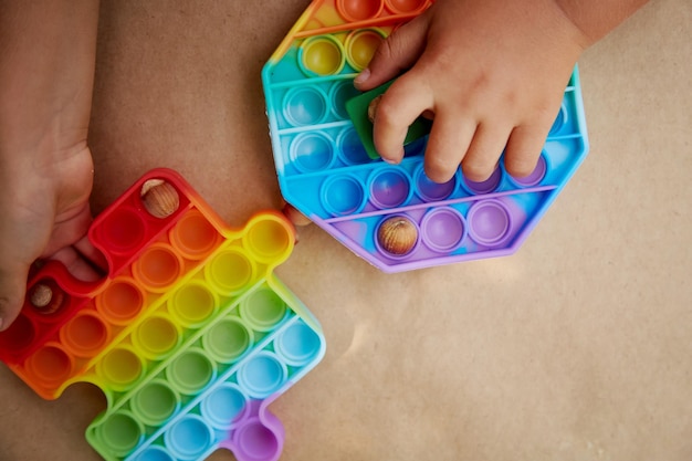 Kid erfand ein Spiel mit trendigem Pop-It-Spielzeug und Haselnüssen Spiel zur Entwicklung der motorischen Fähigkeiten Rainbow sensory zappeln Push it Draufsicht Kopierbereich Hochwertiges Foto