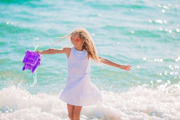 Kid fun. Niña jugando en las olas salpica en playa tropical con cubo y agua