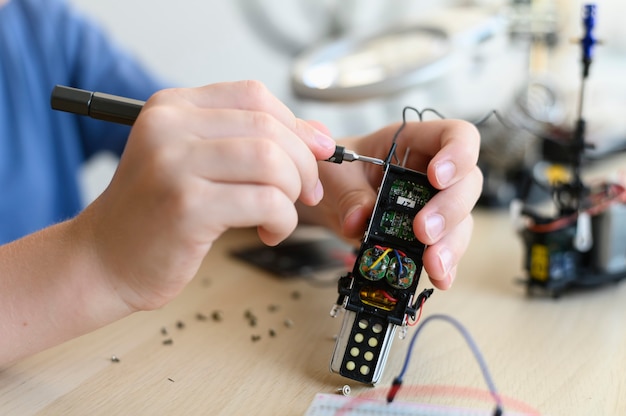 Kid inventor asaltando robot de control de radio de cerca sosteniendo herramientas y robot de bricolaje