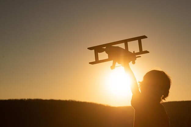 Kid Kinderjunge Pilot Flieger mit Flugzeug träumt davon, im Sommer in der Natur bei Sonnenuntergang zu reisen.