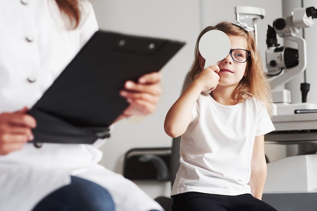 Foto kid luta para ler essas palavras. mulher com documentos testa a acuidade visual de uma menina.
