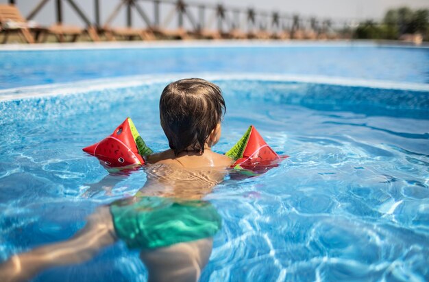 Kid en oversleeves nada en la piscina para niños bajo el sol de verano