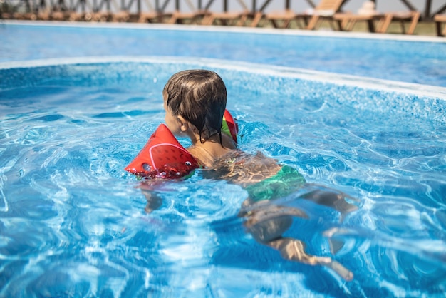 Kid en oversleeves nada en la piscina para niños bajo el sol de verano