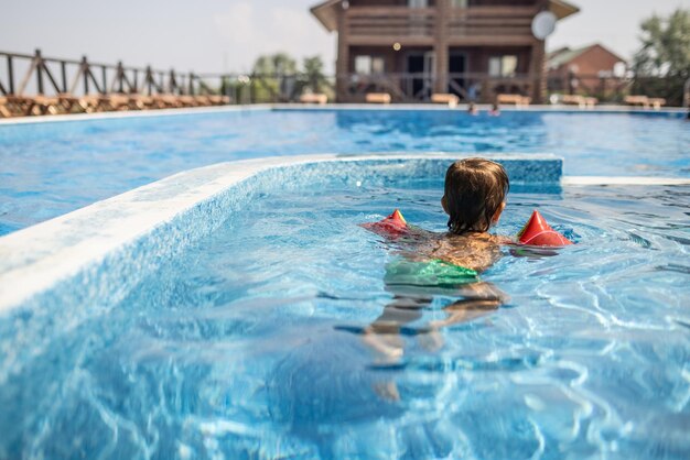 Kid en oversleeves nada en la piscina para niños bajo el sol de verano