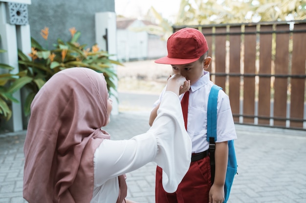 Kid schüttelt und küsst die Hand seiner Mutter vor der Schule