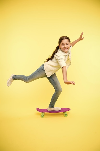 Kid Spaß mit Penny Board Hobby Lieblingsbeschäftigung Kind lächelndes Gesicht stehen auf Skateboard Penny Board niedlich buntes Skateboard für Mädchen Lässt uns reiten Mädchen reiten Penny Board gelben Hintergrund