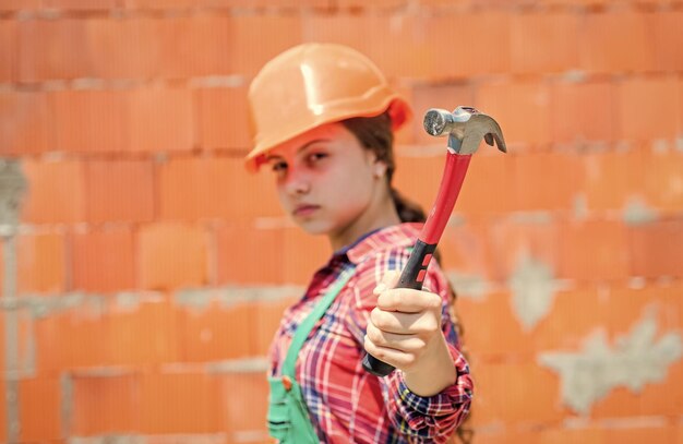 Foto kid wear helm auf der baustelle teen girl builder mit bauwerkzeughammer kind bei der reparatur des arbeitskonzepts der renovierung in der werkstatt beschäftigter professioneller tischler reparatur
