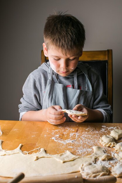 Kidboy haciendo dumplings pierogi varenyky servido con requesón puesto en tamiz cocina nacional de Ucrania producto de panadería casera orgánica natural