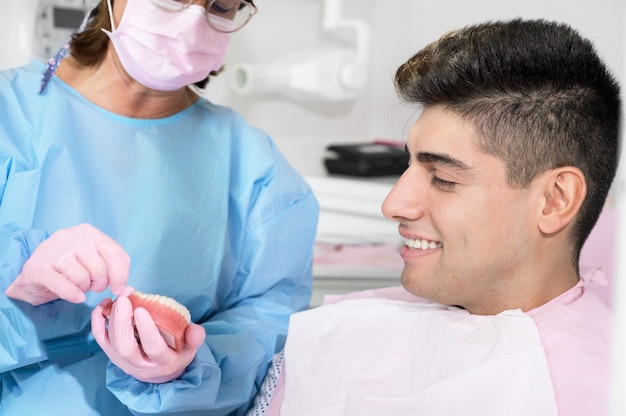 Kieferorthopäde, die einen unsichtbaren Halter für die Zahnausrichtung in der Klinik hält, zeigt dem Patienten moderne Zahntechnik ...