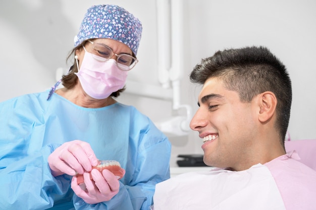 Kieferorthopäde, die einen unsichtbaren Halter für die Zahnausrichtung in der Klinik hält, zeigt dem Patienten moderne Zahntechnik ...