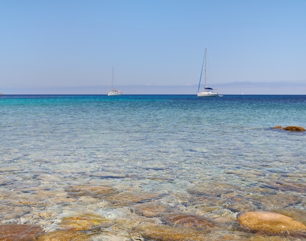 Kieselsteine in klarem Wasser mit Boot am Horizont - Revellata-Korsika