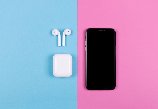 Kiev Ucrania 20181019 Vista superior del iphone XS y Apple AirPods sobre fondo rosa y azul