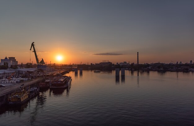 KIEV, Ucrania - 30 de mayo de 2018: Distrito industrial de Kiev en el distrito de Podil. Dnieper y el puerto fluvial. Vista desde el puente Rybalsky atirantado por la noche durante la puesta de sol