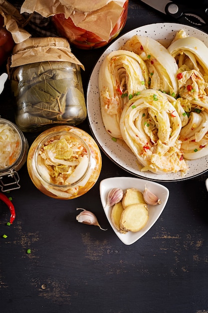 Kimchi de col, tomates marinados, frascos de vidrio agrio de chucrut sobre la mesa de la cocina rústica.