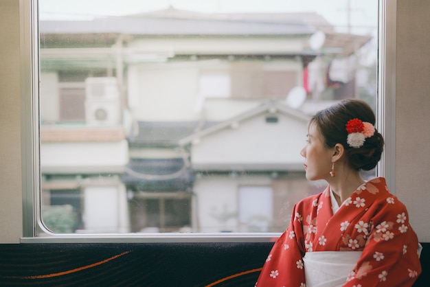 Kimono que lleva de la mujer asiática que viaja por el tren clásico de Japón que se sienta cerca de la ventana