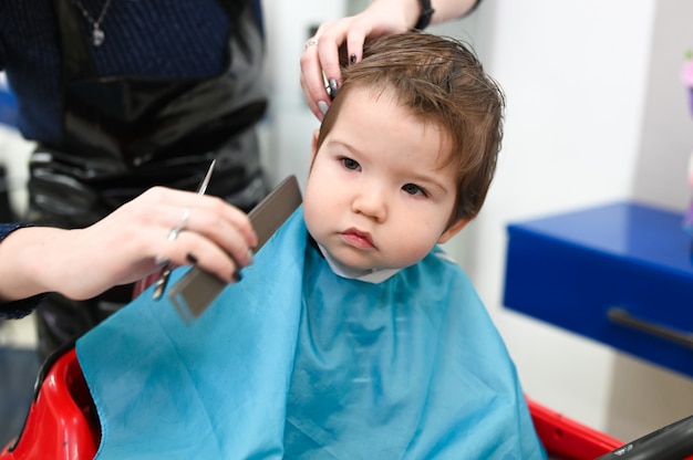 Kind am Friseur Nahaufnahme. Der erste Haarschnitt des Kindes beim Friseur. Baby Haarschnitt Kleinkind.