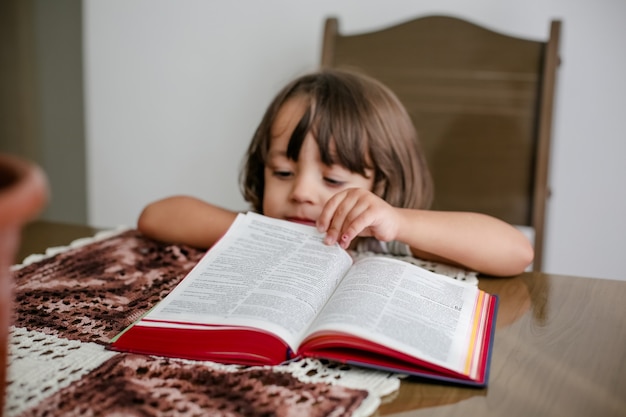 Kind auf dem Tisch, das die Bibel liest und darin blättert