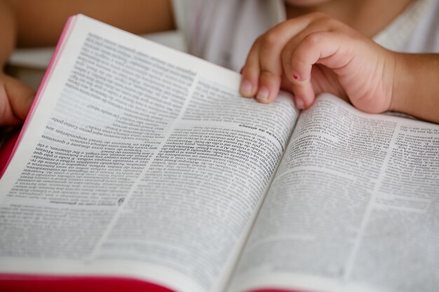 Kind auf dem Tisch, das die Bibel liest und darin blättert