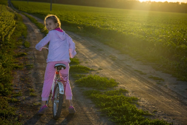 Kind auf einem Fahrrad auf einem Hintergrund der grünen Wiese und mit den Strahlen der Abendsonne