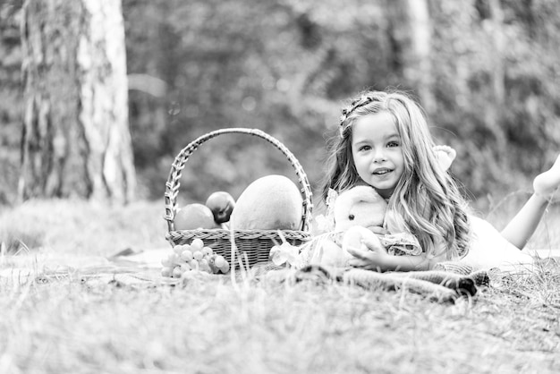 Kind auf Picknick mit Korb, Kind im Herbstpark. Kleines Mädchen umarmt Teddy und genießt die Freizeit.