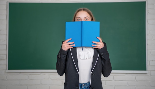 Kind auf Tafelhintergrund versteckt sich hinter Arbeitsbuch in der Schule