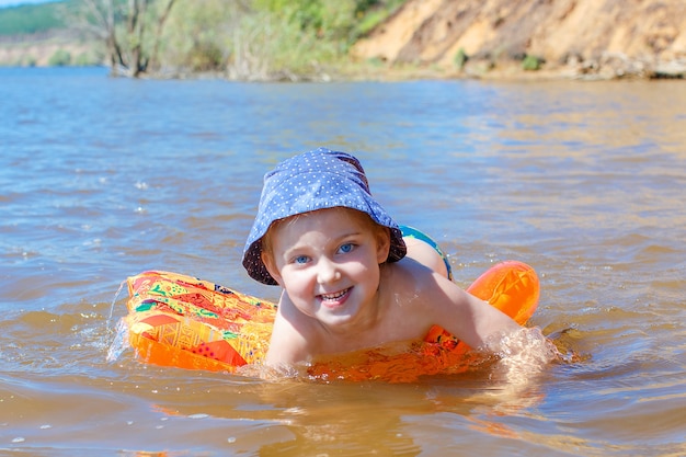 Kind badet auf einer Luftmatratze im Fluss