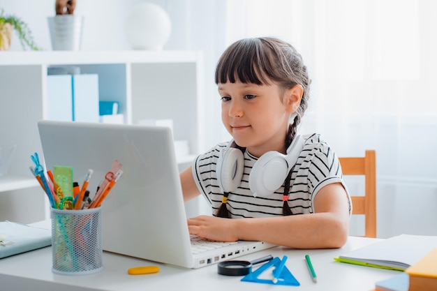 Kind brünette Schülerin lernt Hausaufgaben während einer Online-Stunde zu Hause in einem hellen weißen Raum Schulzeit Online-Bildungskonzept