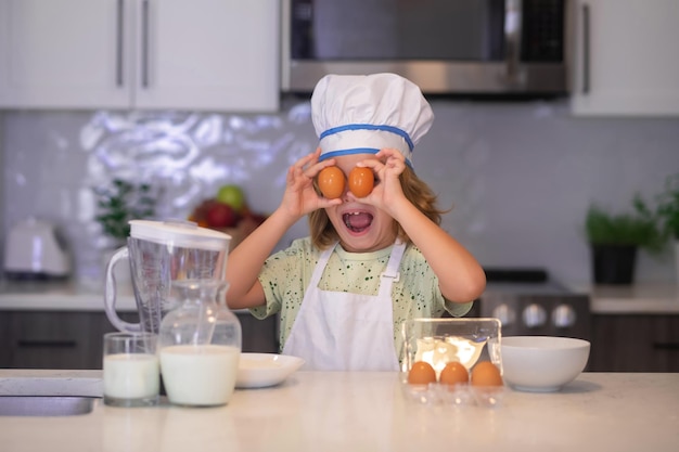 Kind-Chef-Koch mit Eiern Kind in Kochmütze und Schürze, die Zubereitung von Speisen in der Küche Kochen von Kindern Kind Junge mit Schürze und Kochmütze, die eine gesunde Mahlzeit in der Küche zubereiten Kochvorgang