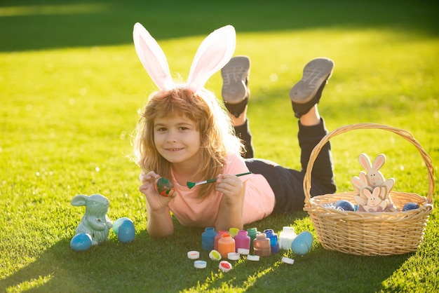 Kind, das auf Gras im Park mit Ostereiern liegt Süßes Kind, das fröhliche Ostern im Park hat