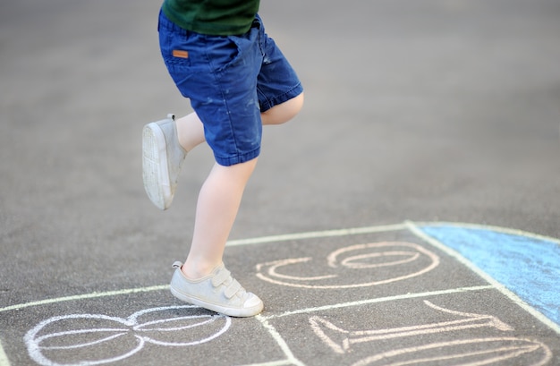 Kind, das draußen Hopse-Spiel auf Spielplatz an einem sonnigen Tag spielt