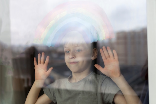 Kind, das durch das Fenster mit gemaltem Regenbogen darauf schaut