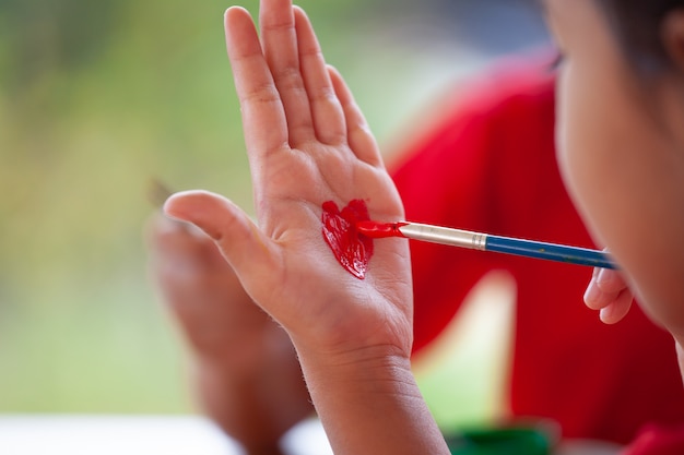 Kind, das ein Herz auf ihrer Hand mit Spaß zeichnet und malt