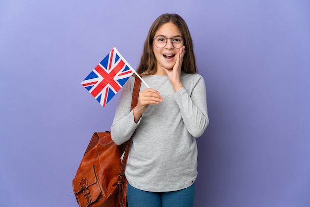 Kind, das eine britische Flagge über isoliertem Hintergrund mit Überraschung und schockiertem Gesichtsausdruck hält