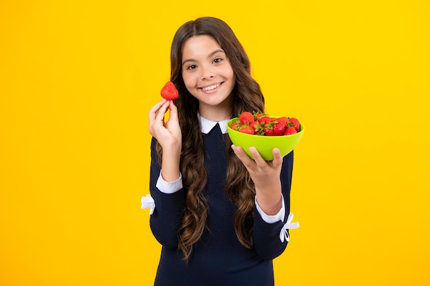 Kind, das eine Erdbeere isst Glückliches lächelndes Teenager-Kind hält Erdbeerschüssel auf gelbem Hintergrund Gesunde natürliche Bio-Vitamin-Lebensmittel für Kinder Erdbeersaison