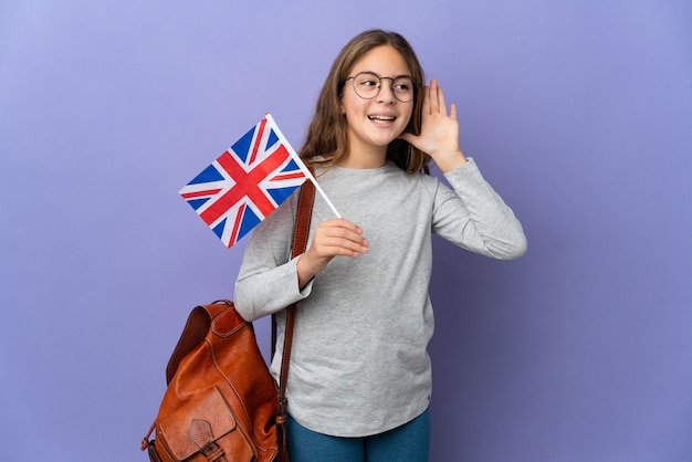 Kind, das eine Flagge des Vereinigten Königreichs über isoliertem Hintergrund hält und etwas hört, indem es die Hand auf das Ohr legt