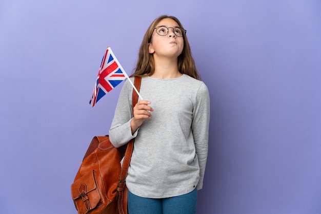 Kind, das eine flagge des vereinigten königreichs über isoliertem hintergrund hält und nach oben schaut