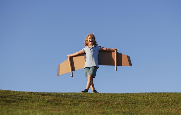 Kind, das im Flugzeug fliegt, machte Handwerk aus Pappflügeln, Junge, der im Freien Traumphantasie spielte