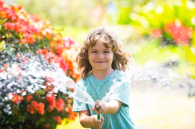 Kind, das im Garten spielt, gießt aus dem Schlauch, macht ein glückliches Kindheitskonzept des Regens