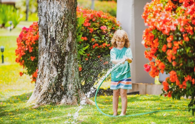 Kind, das im Garten spielt, gießt aus dem Schlauch, macht ein glückliches Kindheitskonzept des Regens