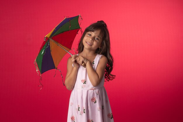 Kind, das im Studiofoto mit rotem Hintergrund mit buntem Regenschirm lächelt.