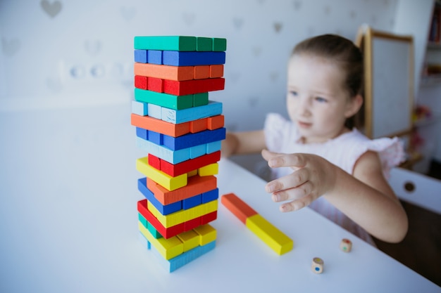 Kind, das mit bunten hölzernen Ziegelsteinen auf dem weißen Tabellenhintergrund spielt