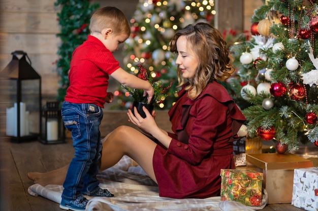 Kind, das Mutter Neujahrsgeschenk nahe Weihnachtsbaum gibt. glückliche Familie im Urlaub. glücklicher Junge und Frau zu Hause am Weihnachtsabend